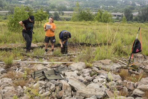 3 Moravian students conduct research in a rocky area of a grassy hill
