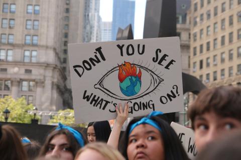 Group of students, one holding a poster that says "Don't You See What's Going On?" with a drawing of Earth with flames