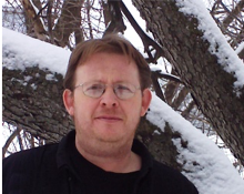 David's headshot- David is standing in fron of a tree covered in snow and is wearing a black sweater