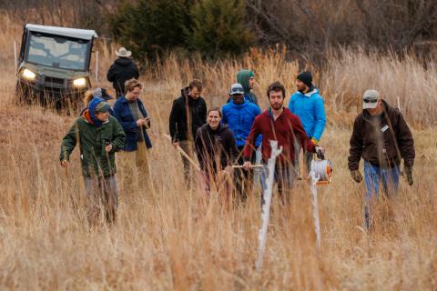11 students and faculty from Yale University walk in a field while conversing and holding technological tools