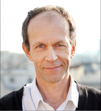 Thierry Dore's headshot. Thierry is wearing a black sweater and standing in front of a blurrd out city. 