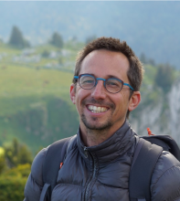 Nicolas Gratiot in a gray jacket and blue glasses in front of a mountain