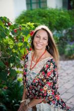 Dina stands in front of some plants wearing a floral dress